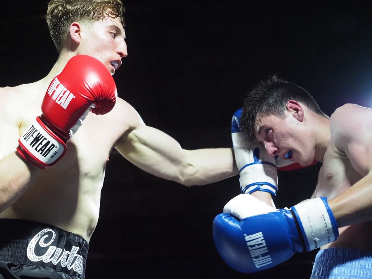 A fighter in red gloves lands a straight punch on his opponent's guard